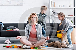 mother meditating in lotus position and looking at camera while naughty kids playing photo