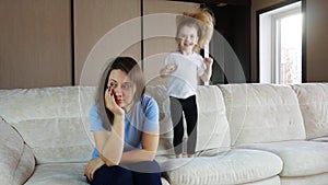 Mother meditating sitting on sofa while active child daughter jumping playing