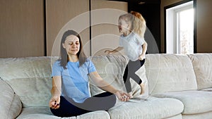 Mother meditating sitting on sofa while active energetic child daughter jumping