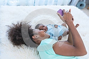 Mother and 1 month old baby newborn son lying on white bed and looking at mobile phone