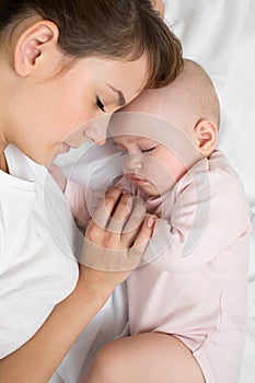 Mother with newborn baby sleeping on the bed at home. Top view, close up.