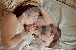 Mother and newborn baby sleeping in bed. Mother kissing baby`s head. Motherhood concept.