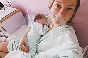 Mother and newborn after childbirth in maternity hospital room. Mother hugging her sleeping newborn baby