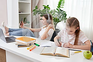 Mother is not helping daughter to do homework while using her smart phone and listening to music with headphones