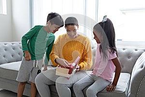 Mother opening a gift box with her children in living room at home