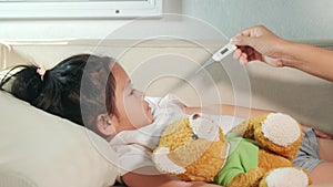 Mother parent checking temperature of her sick daughter with digital thermometer in mouth