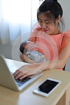 Mother parenting a baby newborn sleeping in home office, businesswoman typing keyboard laptop computer