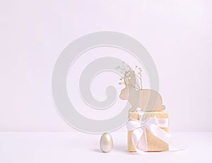 Mother-of-pearl Easter egg and a wooden hare with a hepsophila branch on a gift box on a white background