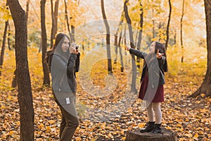 Mother photographer takes pictures of a her daughter in the park in autumn. Hobbies, photo art and leisure concept.