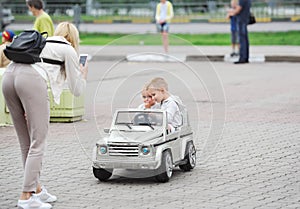 Mother, photographs the small children sitting in the toy car in the city park