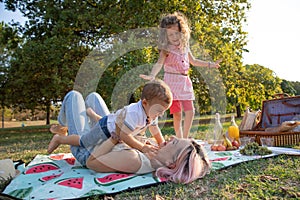 Mother at a picnic plays with her children, lifts her son while her daughter watches