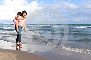 Mother piggybacking her kid on beach, playing together on summer holiday vacation, joyful parent with child boy spending time on