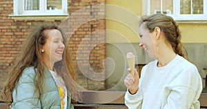 Mother play and spread ice cream on teenage daughter nose when sitting on bench.