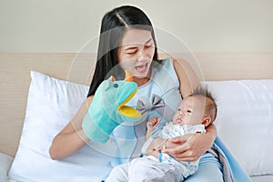 Mother playing animal puppet with her infant baby boy on the bed room at home