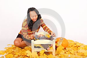 Mother playing with baby boy lying on wooden bed in leaves by pumpkin - Halloween