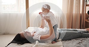 Mother playing with baby daughter sitting on her stomach in bed