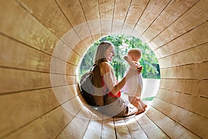 Mother playing with baby in eco-friendly playground. Wooden tunnel for children