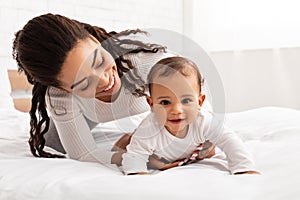 Mother Playing With Baby Helping Her Crawl On Bed Indoor