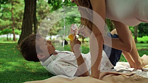 Mother playing with daughter in park. Cheerful girl blowing soap bubbles outside