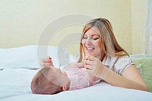 Mother playing with her baby on the bed. Mom smiles to her child