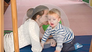 Mother playing with her baby boy in room with colourful blocks, balls, kitchen