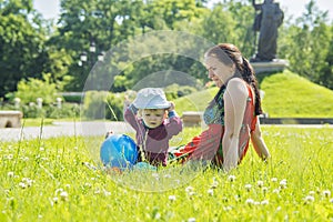 Mother playing with her baby on a great sunny day in a meadow with lots of green grass and wild flowers