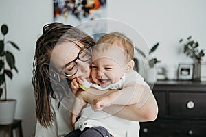 Mother playing with her little baby at home lifestyle concept look. Neutral white clothes clothes, gender neutral