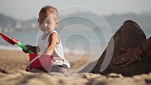 Mother playing with her little daughter on the beach near the water on the sand