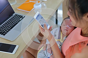 Mother playing mobile phone in business home office with cute baby