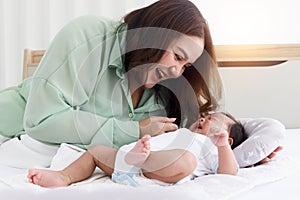 Mother plays with newborn infant baby boy on bed in white bedroom at morning, lovely family mom and child stand time together,