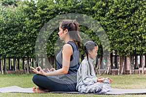 mother practicing doing yoga exercises with her daughter outdoors in meditate pose together