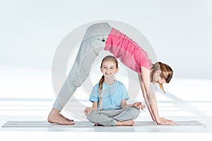 Mother practicing yoga above smiling daughter sitting in lotus position