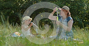 Mother and preschool daughter blow bubbles in the park.