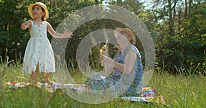 Mother and preschool daughter blow bubbles in the park.
