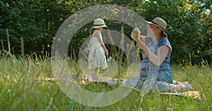 Mother and preschool daughter blow bubbles in the park.