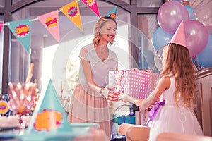 Kind woman smiling and giving birthday present to her daughter