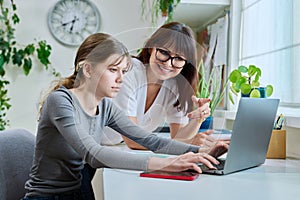 Mother and preteen daughter looking i laptop together, girl typing on keyboard