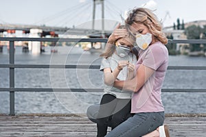 mother in protective mask hugging daughter on bridge air