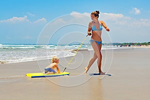 Mother pull baby son on surfing board by sea beach