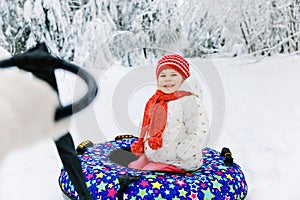 Mother pull little toddler girl on snow tube. Cute little happy child having fun outdoors in winter on colorful tire