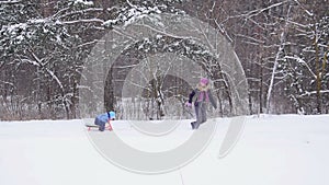 Mother pulling child on sled through snow. Slow motion
