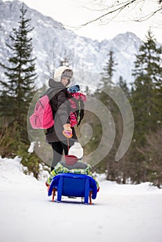 Mother pulling a child through snow on a toboggan