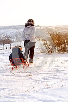 Mother pulling a toboggan with her child in snow
