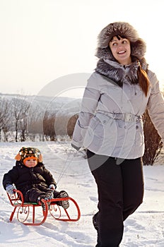 Mother pulling a toboggan with her child in snow