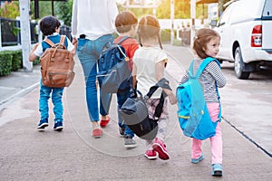 Mother and pupil and kids holding hands going to school in first class with schoolbag or satchel walking to school bus, Parent and