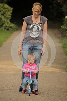 Mother pushing her daughter on a tricycle