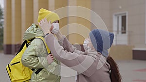 the mother puts medical mask on the little child's nose, the mother escorts the kid to school, protecting the baby from