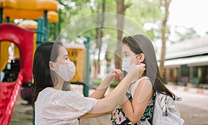 Mother puts a safety mask on daughter face for protection Covid-19 or coronavirus outbreak in village park to prepare go to school
