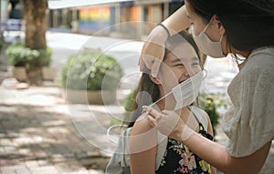 Mother puts a safety mask on daughter face for protection Covid-19 or coronavirus outbreak in village park to prepare go to school