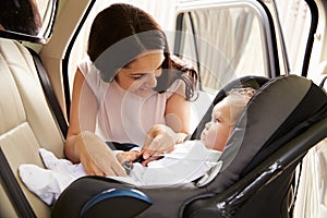 Mother Putting Baby Son Into Car Travel Seat